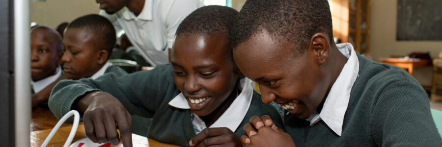 Students Learning at Powering Potential Computer Lab Students in Tanzania smile and work together on a computer in a Powering Potential solar-powered lab.